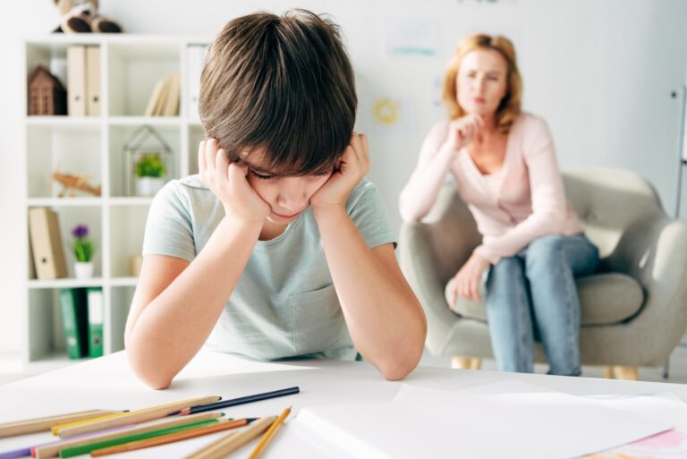 selective focus of sad kid with dyslexia and child psychologist on background
